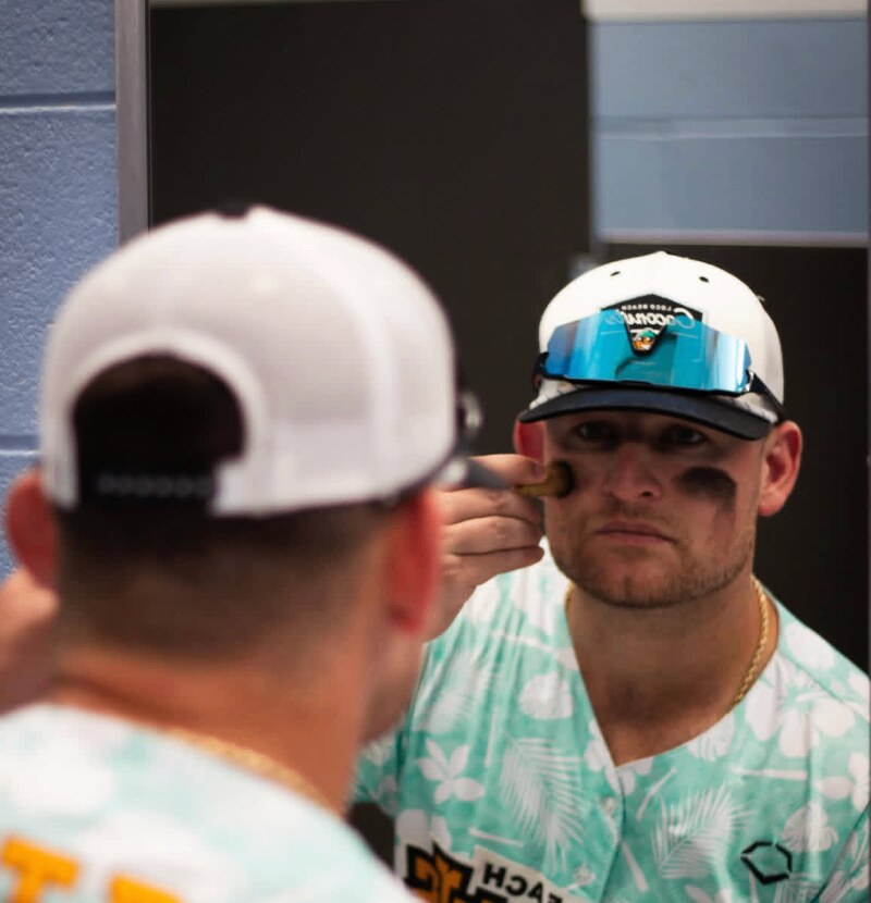 Player applying eye black in the mirror, Squintz shield on the brim